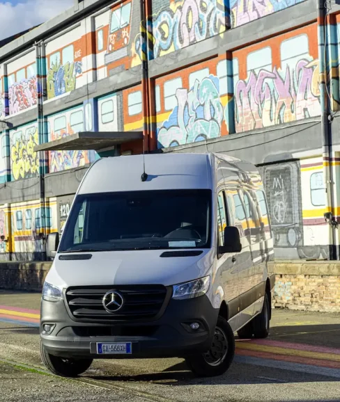 Furgone Mercedes-Benz Sprinter bianco a tetto alto parcheggiato davanti a un edificio industriale con murales colorati